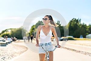 Pretty woman riding bicycle in city park cycle path and street. Bike promenade in summer. Happy smiling cyclist. Stylish trendy.