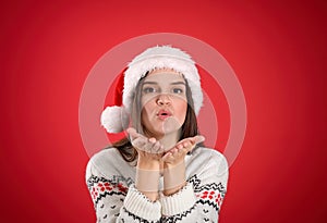 Pretty woman in Santa hat and Christmas sweater blowing kiss on red background