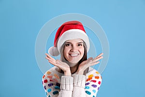 Pretty woman in Santa hat and festive sweater on light blue background