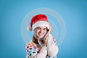 Pretty woman in Santa hat and festive sweater on light blue background