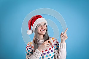 Pretty woman in Santa hat and festive sweater pointing on light blue background