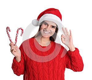 Pretty woman in Santa hat and red sweater holding candy canes on white background