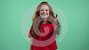 Pretty woman showing thumb up like sign over green studio background. Positive young girl with natural hair smiles to