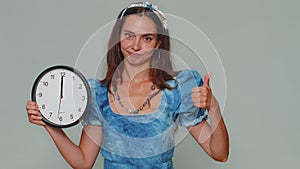 Pretty woman showing time on wall office clock, ok, thumb up, approve, pointing finger at camera