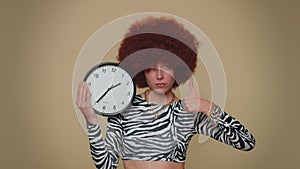 Pretty woman showing time on wall office clock, ok, thumb up, approve, pointing finger at camera