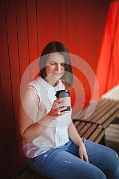 Pretty woman sitting on a bench with a disposable cup of coffee in hand.