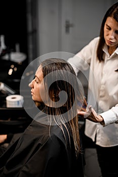 pretty woman is sitting in chair and hairdresser combing her hair with a comb.