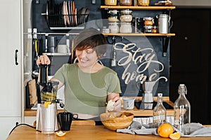 Pretty woman with a smile in her teeth prepares a delicious juice from fresh oranges