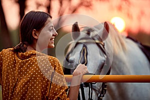 Pretty woman smiling in front of her horse in the sunset