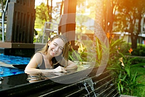 Pretty woman smiling swimming in pool in thailand looking up on sunny day