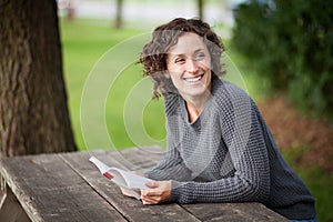 Pretty woman smiling to somebody behind her. She is at a picnic table photo