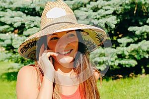 Pretty woman in straw hat speaks via smart phone with relatives