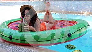 Pretty woman in straw hat and sunglasses lying on inflatable watermelon island in swimming pool