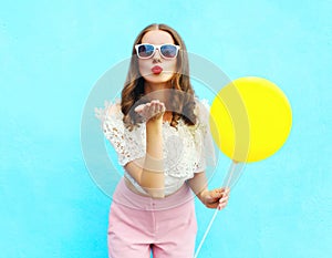 Pretty woman in sunglasses with air balloon sends an air kiss over colorful blue