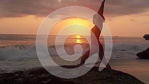 Pretty woman in swimsuit doing yoga on the ocean coast. Silhouette of young girl doing exercises while the waves beat on