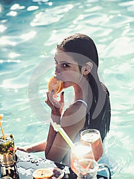 Pretty woman in a swimsuit enjoying cocktail in a swimming pool.