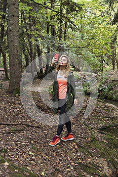 Pretty woman taking pictures while walking in the forest in autumn