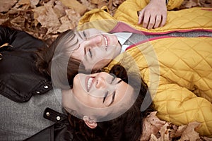Pretty woman and teen girl are posing in autumn park. They are lying on fallen leaves. Beautiful landscape at fall season