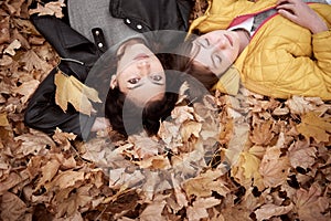 Pretty woman and teen girl are posing in autumn park. They are lying on fallen leaves. Beautiful landscape at fall season