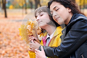 Pretty woman and teen girl are posing with bunch of maple`s leaves in autumn park. They are closing eyes and dreaming. Beautiful