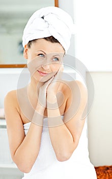 Pretty woman with towel putting cream on her face