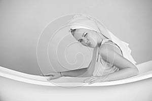 Pretty woman with towel turban sitting in white bathtub