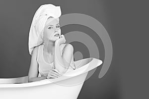 Pretty woman with towel turban sitting in white bathtub