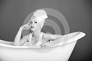 Pretty woman with towel turban sitting in white bathtub