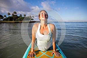 Pretty woman in upward dog pose doing SUP Yoga on the water photo