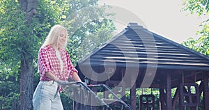 Pretty woman using electric mower while working on backyard