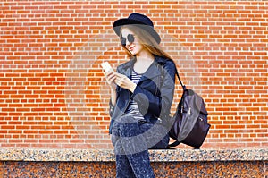 Pretty woman using smartphone in rock black style over bricks