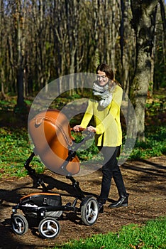 Pretty woman walk with baby pram on sunny outdoor. Woman push stroller on park road. Kid watcher