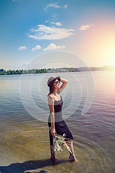 Pretty woman walking along barefoot in evening black dress in city lake