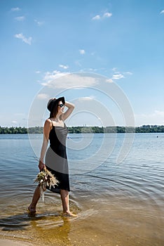 Pretty woman walking along barefoot in evening black dress in city lake