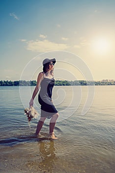 Pretty woman walking along barefoot in evening black dress in city lake