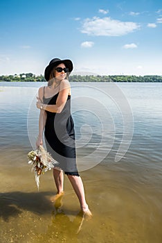 Pretty woman walking along barefoot in evening black dress in city lake