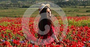 Pretty woman walks in a red field of flowers and touches her hands poppy. Young beautiful woman with charming smile