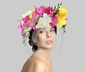 Pretty woman wearing beautiful wreath made of flowers on light grey background