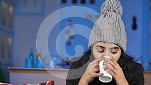 Pretty woman wearing cozy winter clothes blows and drinks a cup of tea / coffee
