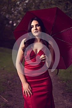 Pretty woman wearing a red dress and holding the red umbrella in the woods