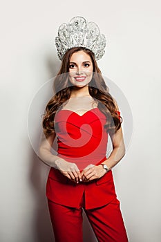 Pretty woman wearing red suit and diamond crown. Smiling model with red lips makeup and long curly hair