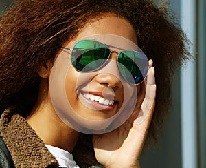 Pretty woman wearing sunglasses with perfect teeth and dark clean skin having rest outdoors
