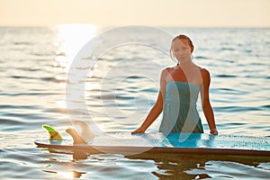 Pretty woman in wet dress posing on sunset with surfboard. Summer time, surfing sport and holiday trip idea, copy space