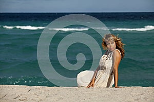 Pretty Woman in white dress sitting on beach