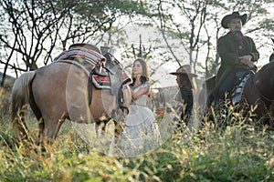 Pretty woman with white dress stand near horse and Asian man with cowboy costume stay on horse that look like he guard or protect