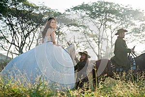 Pretty woman with white dress stay on horse and take care by cowboy girl and man stay beside  in field near village during travel