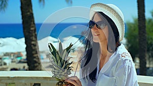 Pretty woman in white hat with tropical cocktail on the beach enjoying sunny weather looking at the ocean view.