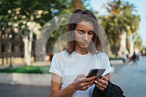 Pretty woman writes message on mobile smartphone while walking Park barcelona on a warm summer day, hipser girl listens to music