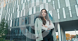 Pretty women with magnificent figure stands in front of modern office building dressed in elegant clothes stilettos