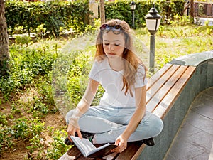 Pretty yaoung girl reading a book on a bench in a park